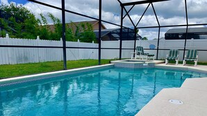 Una piscina con cerca blanca y sillas verdes.