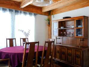 A dining area with a wooden table and chairs, a cabinet with glass doors, and a window with curtains.