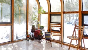 Una veranda luminosa con ampie finestre, una sedia di legno, un tavolino e piante in vaso.