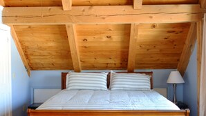 Una camera da letto con soffitto in legno, un letto con biancheria bianca e un comodino con una lampada.