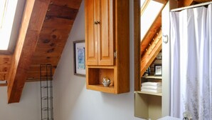 Un bagno con soffitto in legno, lavandino bianco, WC e tenda da doccia.