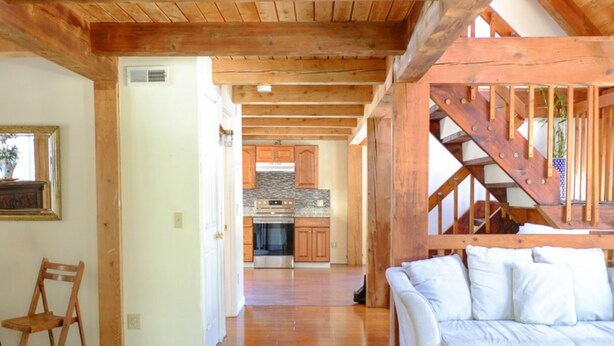 Un'ampia zona giorno con una scala in legno, un divano bianco e una cucina sullo sfondo.