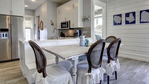 A modern kitchen with white cabinetry, a central island, and a dining area with four chairs. - Designer Beach Condo w/ Bonus Beach Gear & Amenity Access@Cinnamon Shore (Port Aransas)