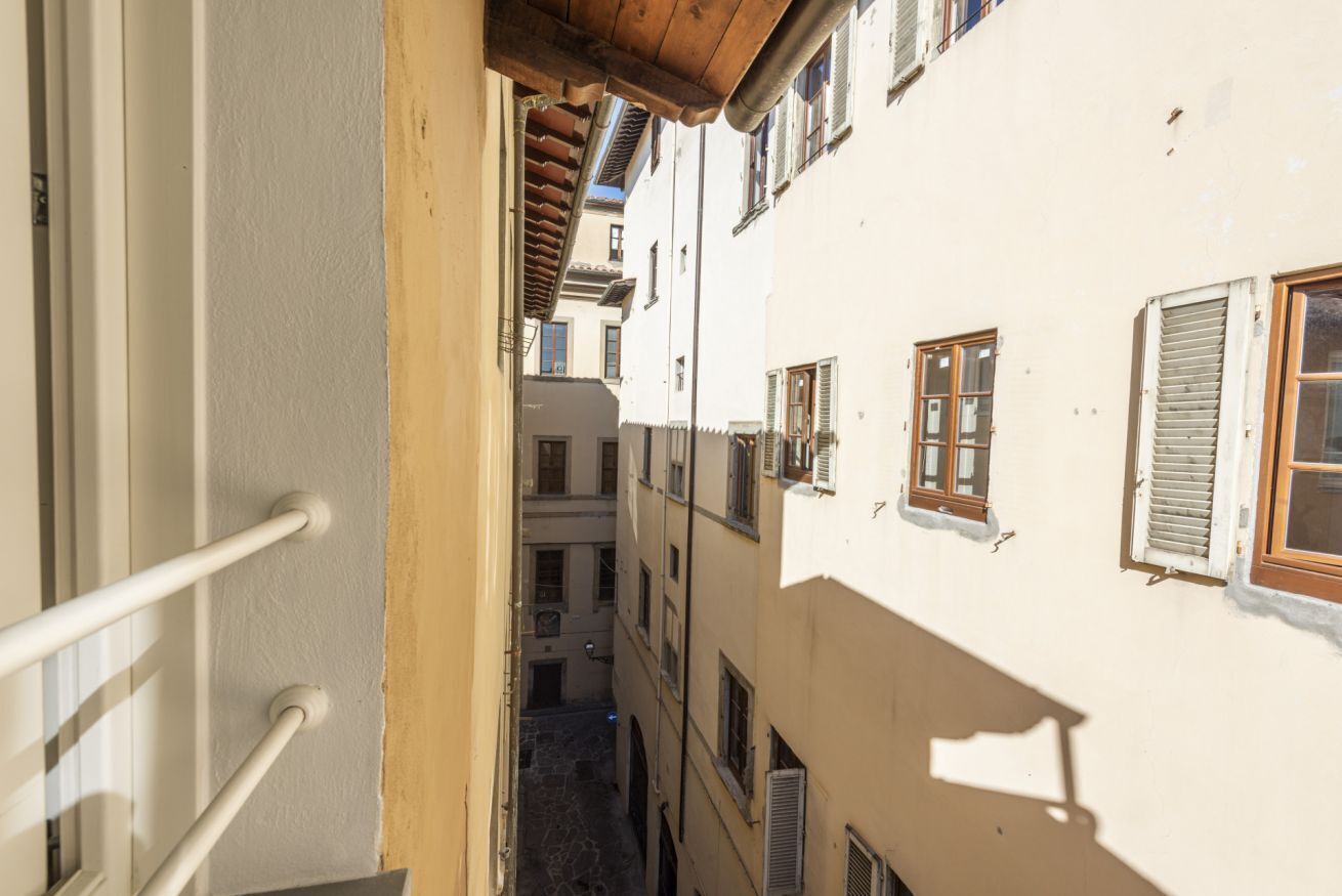 Un estrecho callejón entre edificios con balcones, techo de madera y pared blanca con una puerta.