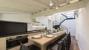 Una cocina moderna con una isla central, horno empotrado y una escalera que sube a un nivel superior.
