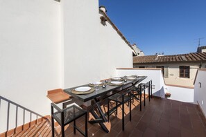 Une terrasse sur le toit avec une table à manger pour quatre personnes, entourée de chaises, et un petit coin salon avec un banc.