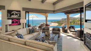 Un salón amplio con un sofá beige grande, una mesa de centro y vistas al océano y a una piscina.