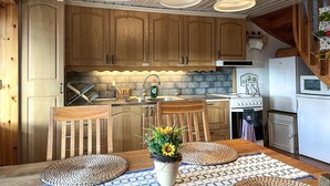 Cocina con armarios de madera, estufa, fregadero y refrigerador. Hay tres lámparas colgantes sobre la encimera.
