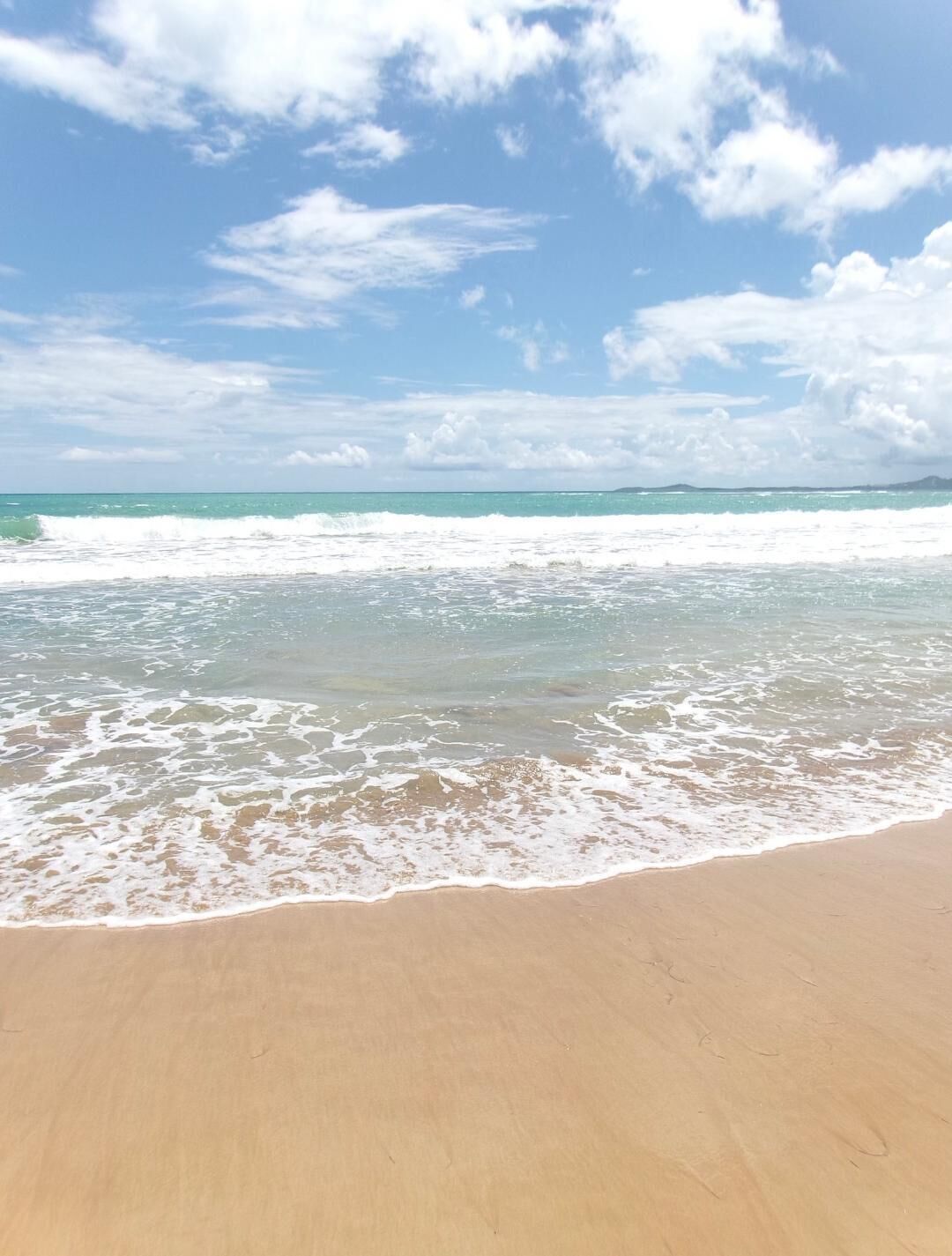 A beach with waves, clear sky, and distant land.