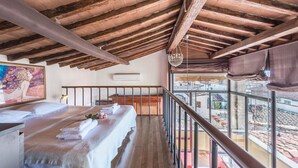 Ein Zimmer mit Holzboden, einem Bett mit weißen Leinen, einem Gemälde an der Wand und einem Balkon mit Blick.