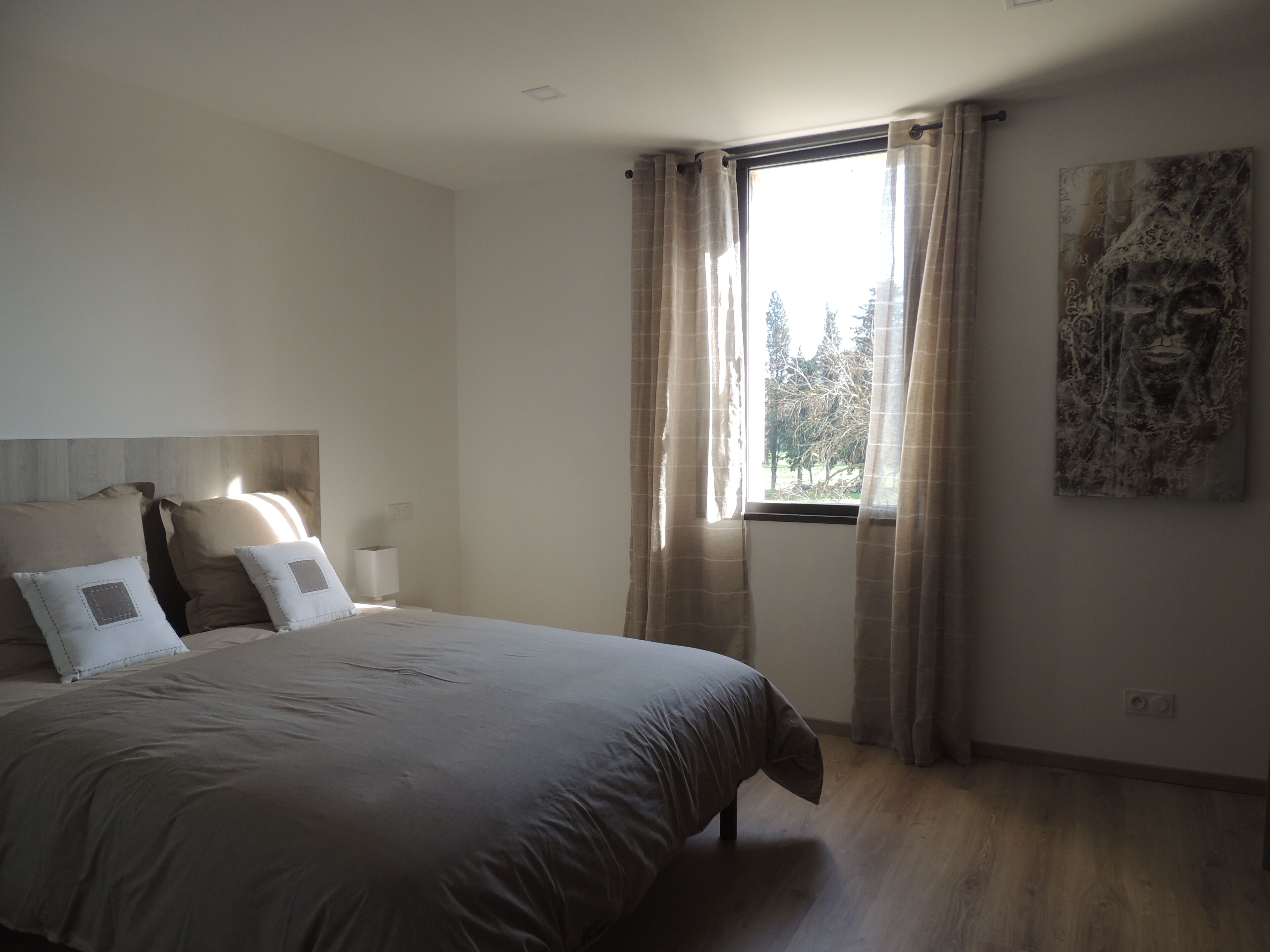 A bedroom with a large bed, a window with curtains, and a painting on the wall.
