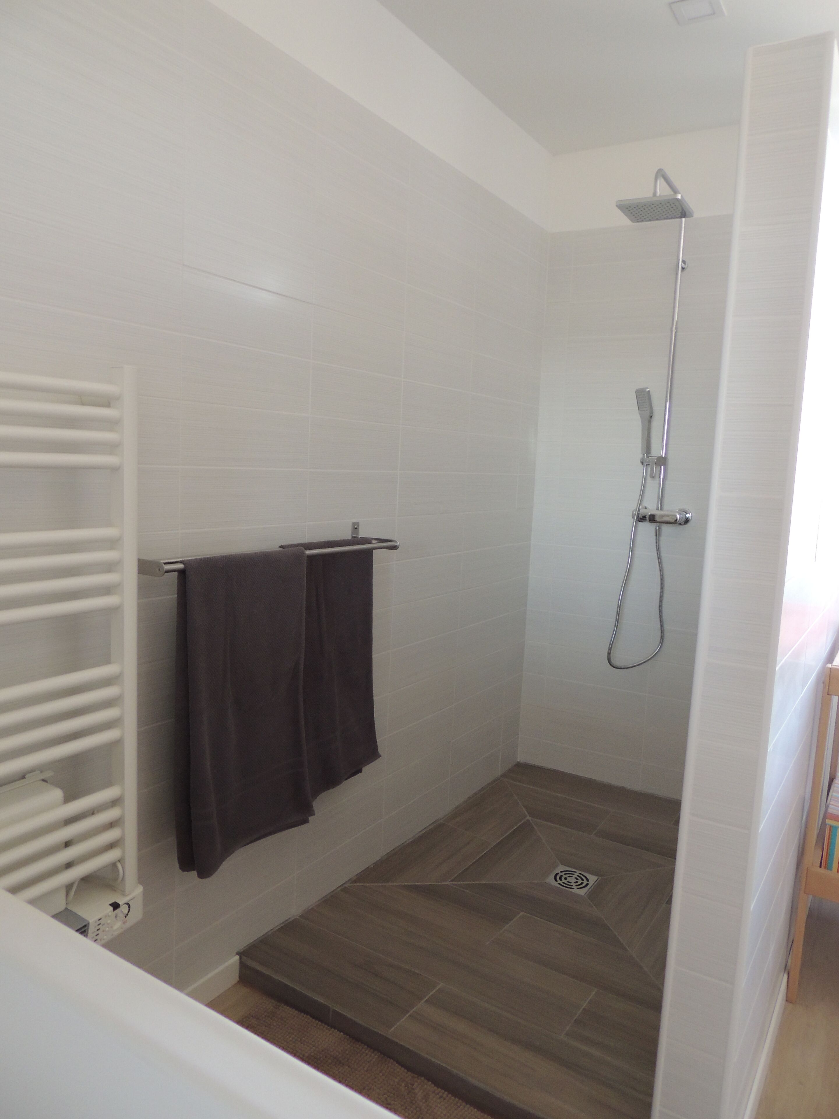 A shower area with a showerhead, a towel rack with two towels, and a wooden floor.