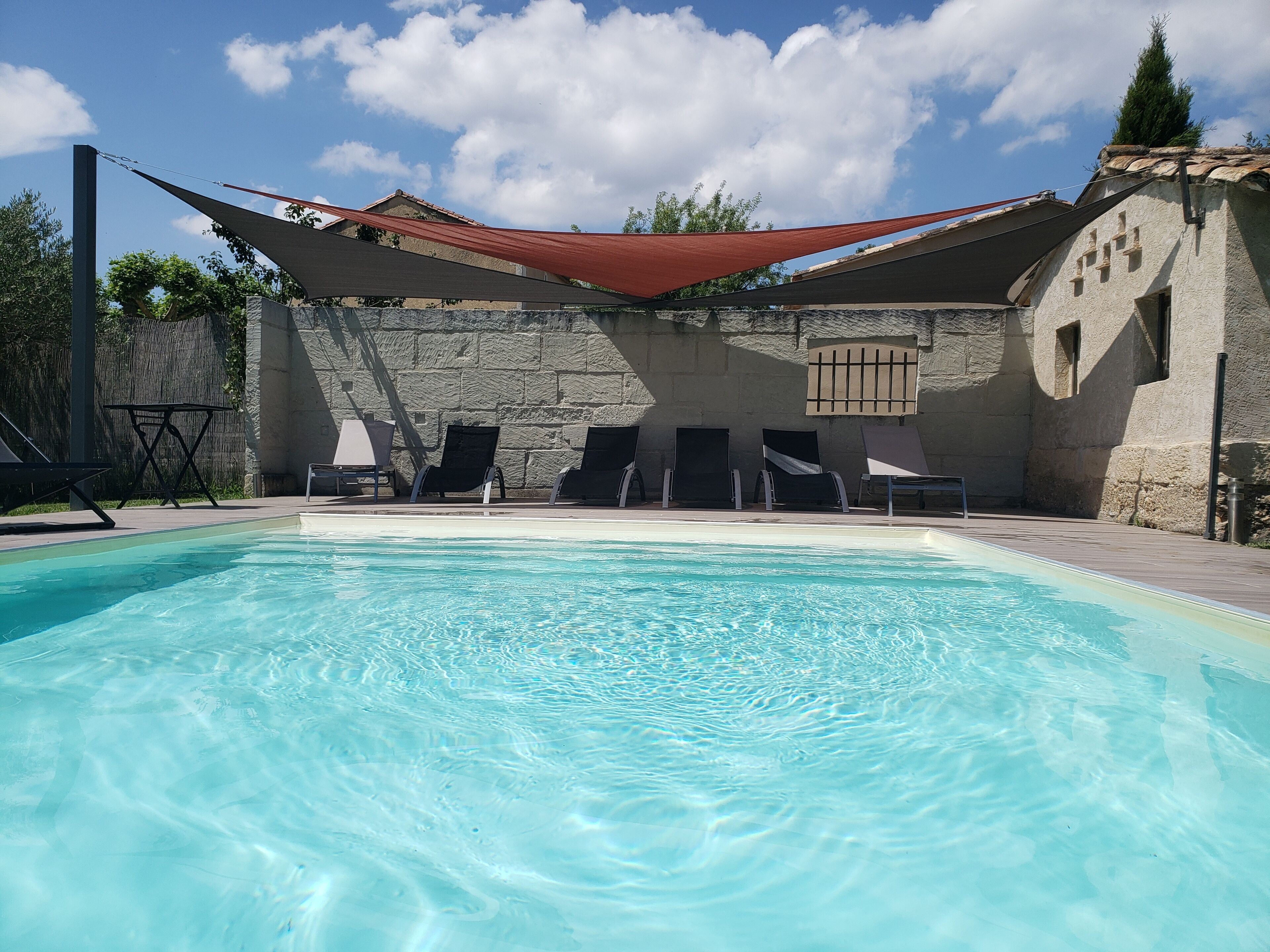 Una piscina con estructuras de sombrillas, sillas de descanso y un edificio de piedra al fondo.