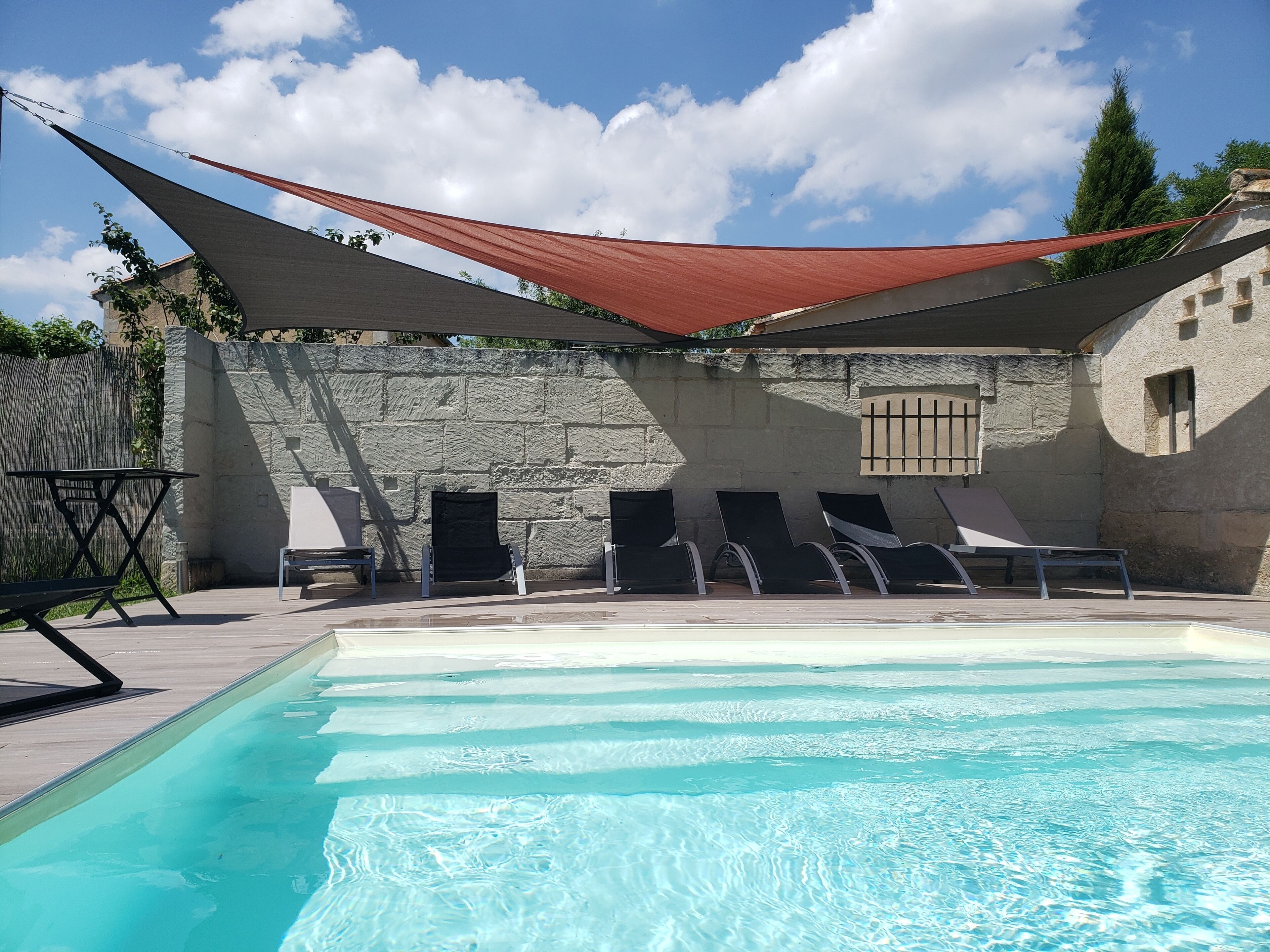 A swimming pool with lounge chairs and a shaded area, surrounded by stone walls and a clear sky.