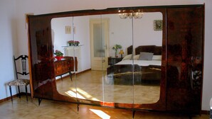 Una habitación con un espejo grande, un armario de madera, una cama, una mesita de noche y una silla.