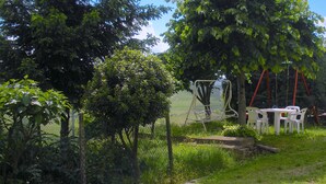 Un espacio al aire libre con césped, un columpio, una mesa con sillas y una cerca.