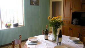Comedor con una mesa dispuesta para cuatro, mantel blanco, platos, cubiertos y un jarrón con flores amarillas.