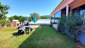 A patio area with outdoor furniture and a large umbrella, surrounded by a well-maintained lawn and a building with large windows. - Home for Nature Tourism, Madeira Island LAURISHOUSE, Nature and Sea (Prazeres)