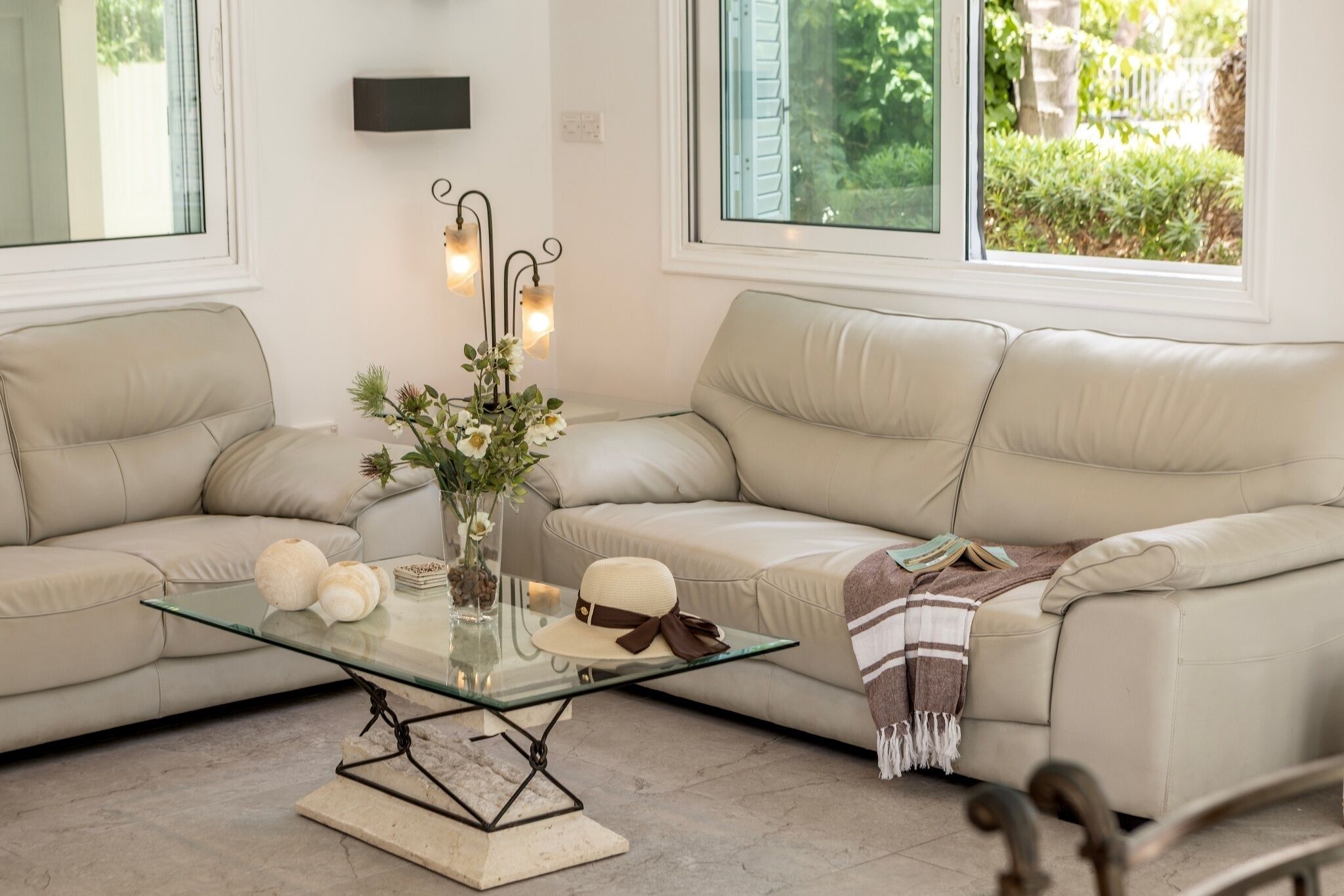 Una sala moderna con un sofá color beige, una mesa de centro de vidrio y un jarrón con flores.
