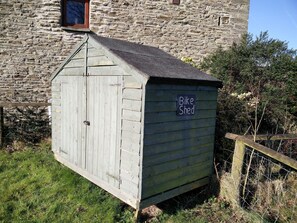 Un abri en bois portant l’inscription « Local à vélos », avec un toit en pente, situé devant un bâtiment en pierre.
