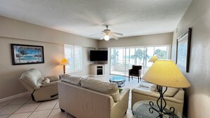 A living room with a sofa, armchairs, a TV, and a glass table. - Island House Beach Resort 13N (Siesta Key)