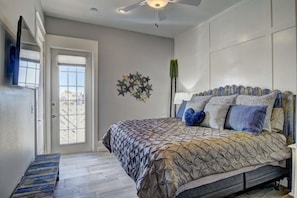 Relax in this serene bedroom with a large bed and ceiling fan, featuring a geometric patterned bedspread and a comfortable bench.