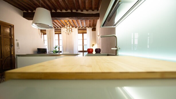 Una cocina con mostrador de madera, lámpara colgante y ventana con cortinas.
