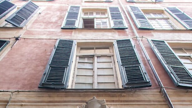 A building facade with multiple windows, some with shutters, and a central decorative element above the entrance. - Ostellin Genova Hostel (Genoa)