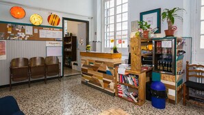 A reception area with a wooden reception desk, a bulletin board, a bookshelf, and a refrigerator. - Ostellin Genova Hostel (Genoa)