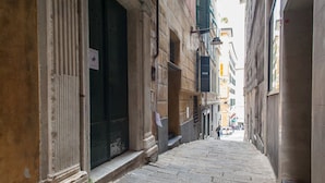 A narrow stone-paved alleyway flanked by buildings with large windows and doors. - Ostellin Genova Hostel (Genoa)
