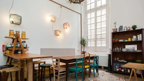 A cozy dining area with a wooden table and chairs, a patterned rug, and a bookshelf with various items. - Ostellin Genova Hostel (Genoa)