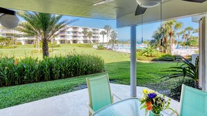A glass table with chairs and a vase of flowers on a balcony overlooking a pool and a building with balconies. - CRC 1108 - Ground Floor Condo Easy Pool Access (St Augustine)