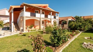 A two-story house with a stone facade, a tiled roof, and a well-maintained garden with various plants and a small statue. - 1 bedroom nice apartment in Podgradina (Podgradina)