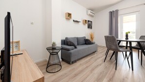 A modern living room with a grey sofa, a round black side table, a wooden dining table with chairs, and a TV on the left. - 1 bedroom nice apartment in Podgradina (Podgradina)