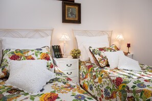 A double bed with floral bedding, two bedside tables with lamps, a small vase with flowers, and a framed picture on the wall. - Fully Serviced Beachfront Extravagance- Heated Pool, Jacuzzi, Mesmerizing Sunset (Bobovisca na moru)