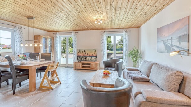 A spacious living area with a wooden ceiling, a dining table with chairs, a sofa, and a painting on the wall. - Ferienhaus 4 Altefähr (Altefähr/Rügen)