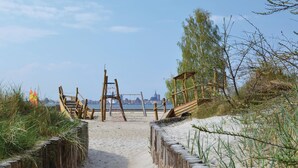 A beach path leading to a wooden structure with a swing set, surrounded by sand and vegetation. - Ferienhaus 4 Altefähr (Altefähr/Rügen)