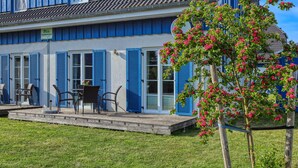 A building with blue shutters, a patio with chairs, and a flower tree. - Ferienhaus 4 Altefähr (Altefähr/Rügen)
