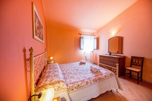 A bedroom with a bed, dresser, chair, and a window with curtains.