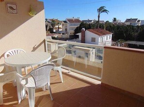 Un balcone con tavolo e sedie, una ringhiera in vetro e vista su case e alberi vicini.