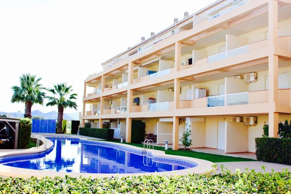 Un hotel a più piani con piscina, balconi e palme.