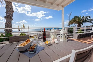 Une terrasse en bois avec une table dressée pour un repas, offrant une vue sur l’océan.