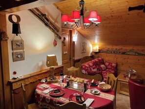 A cozy wooden cabin interior with a dining area, a wooden staircase, and a bed with red bedding.