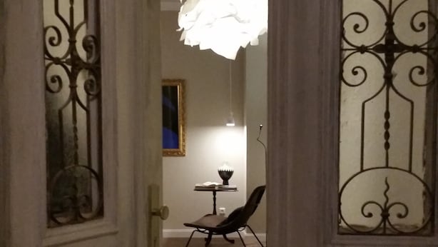 Una vista interna di una stanza con pavimento in legno, un tavolo con una lampada e una sedia.
