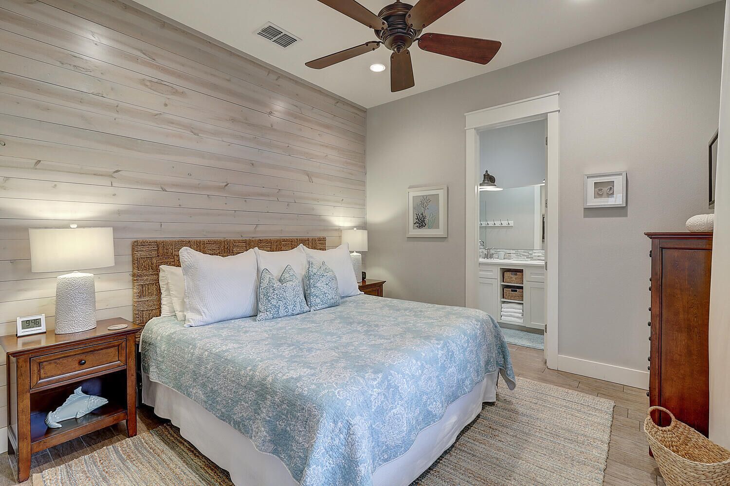 A bedroom with a wooden ceiling, a bed with a blue patterned bedspread, a nightstand with a lamp, a wooden cabinet, and a ceiling fan.