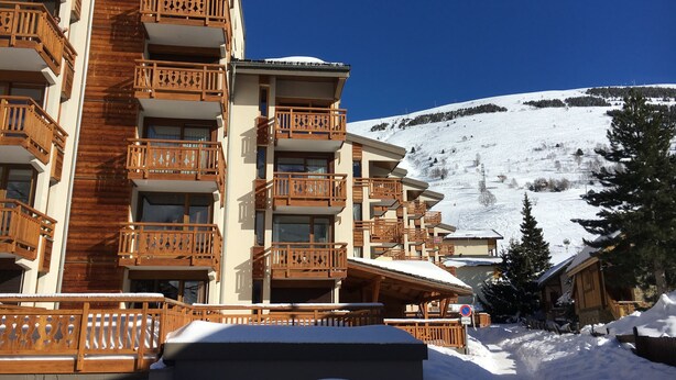 A multi-story hotel with wooden balconies and a snowy mountain backdrop. - T2 / 3, heart of resort, bottom of slopes, parking, 30m3 + 100m2 terrace (Mont-de-Lans)