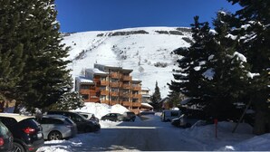 A snow-covered parking area with a building in the background. - T2 / 3, heart of resort, bottom of slopes, parking, 30m3 + 100m2 terrace (Mont-de-Lans)