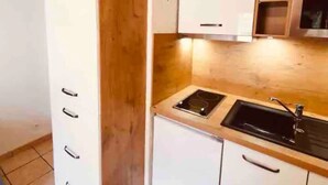 A compact kitchen with white cabinets, a double sink, and wooden ceiling beams. - T2 / 3, heart of resort, bottom of slopes, parking, 30m3 + 100m2 terrace (Mont-de-Lans)