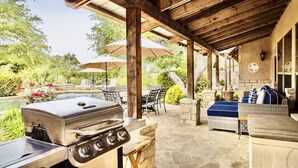 En udendørs patio med grill, stensæder og parasoller.