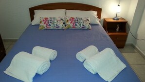 Una cama bien tendida con ropa de cama azul, dos toallas blancas enrolladas y una almohada floral.